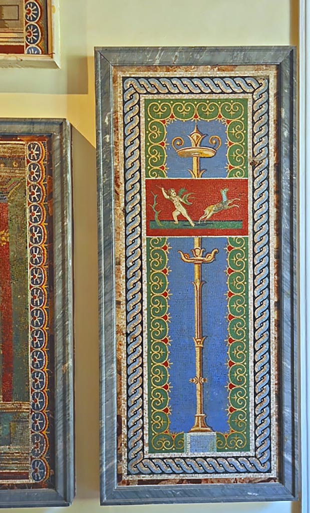 VI.17.36 Pompeii. September 2024. 
One of two mosaic wall panels, now in Naples Archaeological Museum. Inv. no. 10012 and 10013.
Photo courtesy of Giuseppe Ciaramella.
According to the information card –
Mosaic wall panels made from polychrome glass paste tesserae on a light blue background with a gilt candelabrum.
Above, a cupid hunting a deer is depicted within a small panel with a red background, enclosed within a double frame, the outer one with an interlaced pattern and the inner one with plant motifs. (Third quarter of the Ist century AD).
(Pannelli parietali a mosaico di tessere policromo in pasta vitrea su fondo azzurro, con candelabro dorato. In alto, all’interno di un quadretto a fondo rosso, delimitato da una doppia cornice, esterna a treccia, interna a motivi vegetale, e raffigurato un erote che caccia un cervo. 
Terzo quarto del I secolo d.C.)

