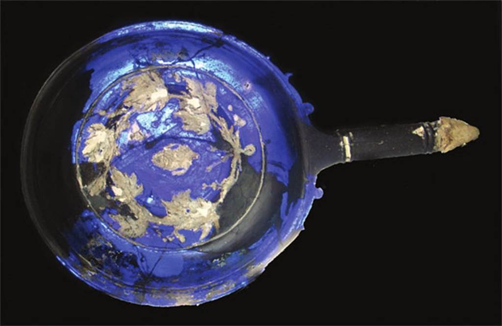 VII.4.62 Pompeii. Tablinum 8, cameo glass patera. The interior of the Patera in white decoration shows a sacred knot with bunches of flowers and sacred ribbons. It was found scattered in many fragments near the room to the right of the tablinum of VII.4.59 Casa della Parete Nera and the room of the adjoining VII.4.62 Casa delle Forme di Creta. Now in Naples Archaeological Museum. Inventory number 1843.