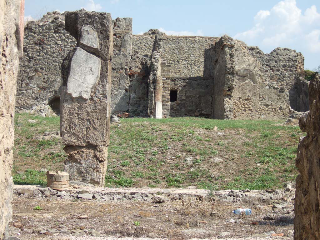 VII.6.38 Pompeii. September 2005.
Looking east across portico towards site of exedra/oecus or tablinum, in lower centre, and VII.6.28 in the background.
According to NdS (1910) -
“On the eastern portico of the peristyle, Exedra 23 opened in all its width, spacious and elegant, with two columns, between the jambs (once covered with wood) which supported the architrave. The room was therefore not closed by shutters, and the doorway lacked a threshold, whose place was occupied by the same flooring as the whole room, formed of cocciopesto with pieces of various coloured marble, inlaid here and there.
The square-shaped room was divided from the side rooms only by thin walls, now fallen, and bore a beautiful painted decoration, now preserved only at the bottom of the facing wall. From this little we see, that the wall showed three large rectangles, the central red and the sides yellow, divided by wide bands probably black, and lower however purple/peacock blue, showing perhaps fantastic architectures, and leaning (what you can see) on two pedestals, each consisting of a forepart of the general zoccolo of the wall. This zoccolo/plinth was black with a purple/peacock blue squaring in the central area, and purple/peacock blue with black squaring in the side areas. Of these three panels, the first one showed a very damaged mask in prospect, perhaps of a female with a kind of pine on top, from which two swirls of floral scrolls come out, all yellow. Each of the other two showed a dolphin. Under this zoccolo was another lesser painting in imitation of slabs of inlaid coloured marble.
In the south wall, today as I have said, destroyed, would have been two doorways, which gave access to small rooms 25 and 26.”
See Notizie degli Scavi di Antichità, 1910, p.446-453.