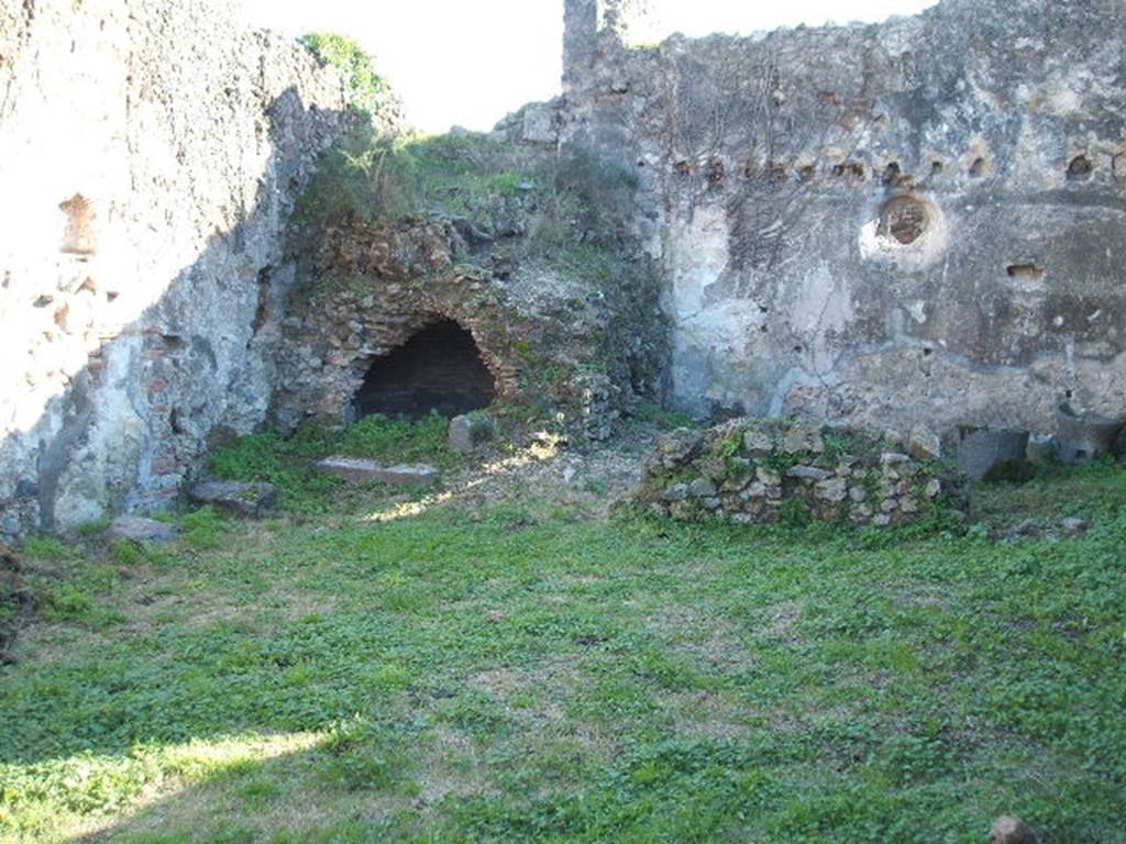 VII.12.13 Pompeii. December 2004. Lararium nNiche on east wall in front of oven in south east corner. Two mills can be seen in the bakery area to the right of the oven.