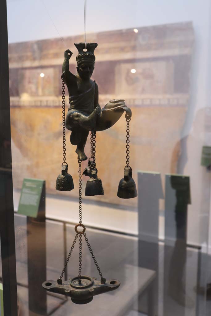 VIII.1.4 Pompeii. February 2021.
Bronze lamp with statuette of a satyr with a phallus from which small bells hang, found in I.6.3.
Photo courtesy of Fabien Bièvre-Perrin (CC BY-NC-SA).