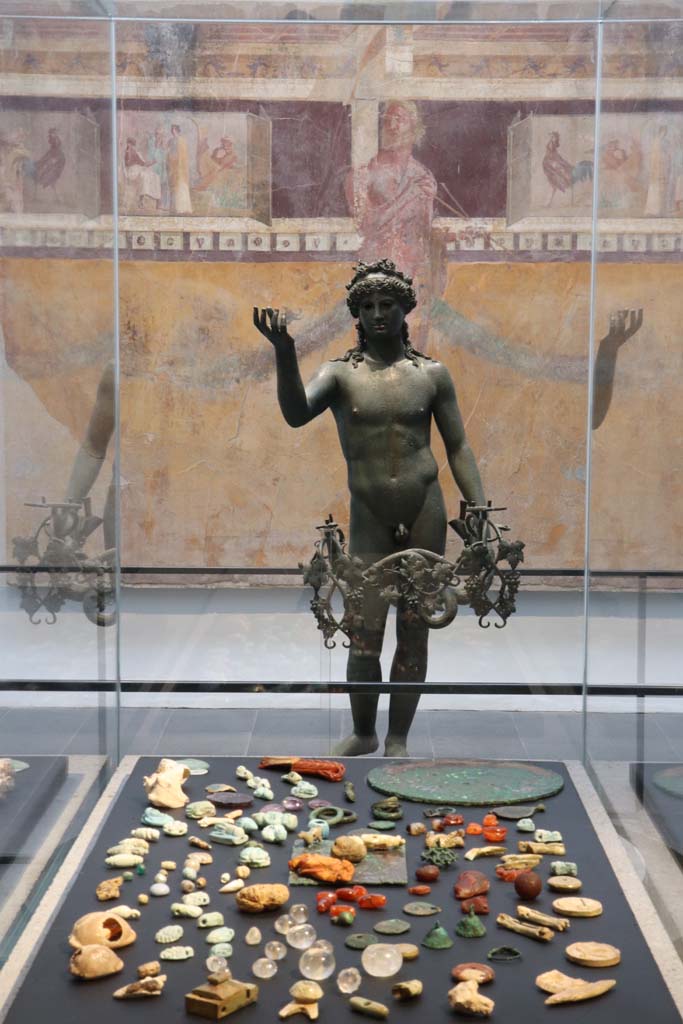 VIII.1.4 Pompeii. February 2021.
Looking across amulets and gems found in V.3, House with Garden, towards bronze Ephebus lamp from VII.16.19/22.
At the rear, is part of the painted wall from the oecus/triclinium of I.6.2.
Photo courtesy of Fabien Bièvre-Perrin (CC BY-NC-SA).