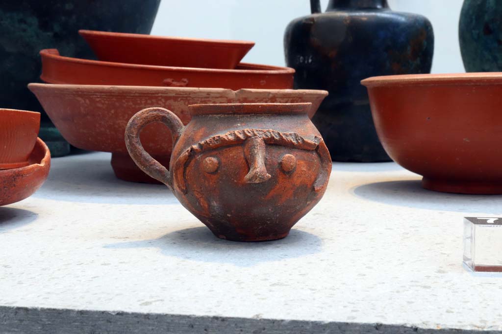 VIII.1.4 Pompeii. February 2021.
Beaker decorated with indentations and a human face together with red ware plates and bowls, from I.10.4, House of Menander.
Photo courtesy of Fabien Bièvre-Perrin (CC BY-NC-SA).