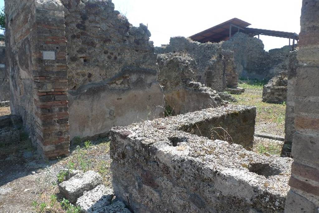 IX.7.22 Pompeii. July 2010. Looking south-east across remains of counter. 
Photo courtesy of Michael Binns.
According to Mau, the podium was covered in stucco, red at the front, and rough and reddish at the rear.
The top had been covered with slabs of marble, which were missing.
On the 30th October 1880, six amphorae with inscriptions were found here.
Also found was a broken amphora containing some lentils.
On the 4th February 1881, in the presence of Granduca Nichola di Russia, were found: 
• The base of an amphora with unidentifiable burnt material.
• A terracotta lamp 
• 3 glass bottles and fragments of a fourth
• Part of the bronze fittings of a chest
• An iron hoe, 11 iron keys and small iron anvil
• 2 bone dies (for game of dice) 
• A glass-paste amulet representing a small herm. 
See Notizie degli Scavi di Antichità, 1880, p.400, 1881, p. 61-2.
See Mau in BdI, 1882, p. 193.
