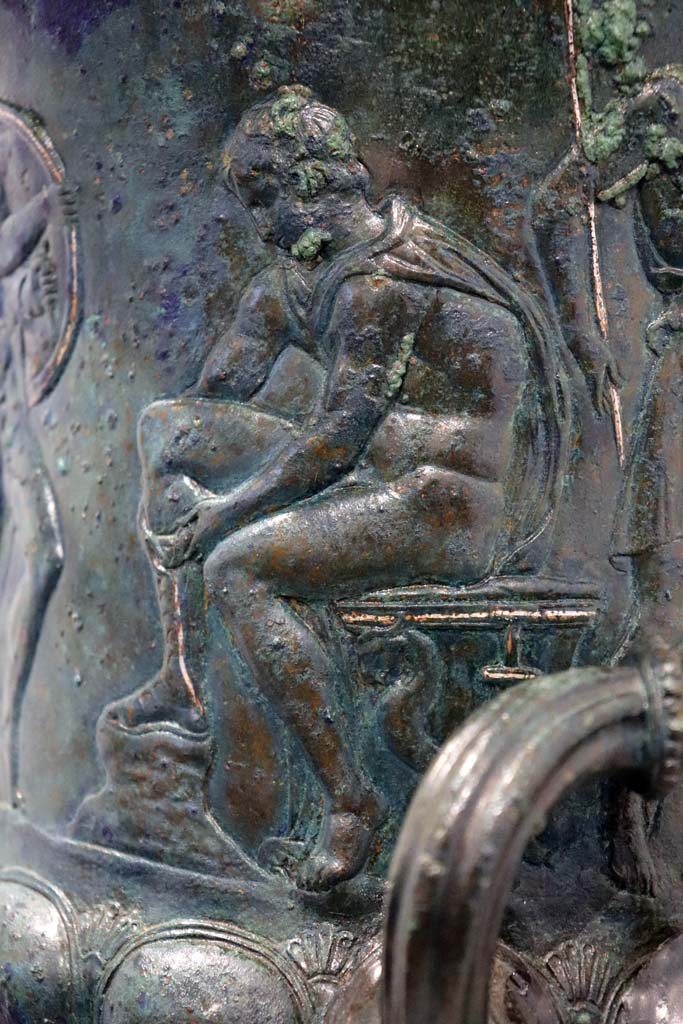 IX.13.1-3 Pompeii. February 2021.
Bronze krater with scenes in relief, found in triclinium, on display in Antiquarium, VIII.1.4.
According to the description card in the Antiquarium -
The bronze krater was decorated with eight armed male figures, six standing and two sitting.
Detail of one of the seated figures tying his shoelaces.
Photo courtesy of Fabien Bièvre-Perrin (CC BY-NC-SA).