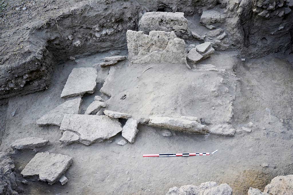 The collapsed slabs of burial SP30055 (HGE31A) being excavated. Taken from the east.
Photo © B. Lemaire, EFR/CNRS.
Burial SP30055, shows elements of the fractured and fallen wall slabs (Fig. 24).
It was a box burial consisting of four monolithic slabs of Sarno limestone placed in the field, delimiting a space in which the deceased and the offerings were placed.
The levels in place that have come down to us allow us to put forward the hypothesis that the burial is installed in the substratum, most probably with the digging of a pit whose limits are represented by the blocks forming the burial.
The slabs on the short sides are enclosed by those on the long sides, forming a box and defining a rectangular structure of 2.25 m by 1.40 m (maximum), oriented north-east/south-west.
The north-western wall, which is better preserved (31.94 m s.l.m.), makes it possible to restore the height and thus the internal space of the tomb: 1.94 m by 0.98 m, for a height of 1.08 m.
(See CEFR 1581 and below) Para 42, Fig. 24.
Les dalles effondrées de la sépulture SP30055 en cours de fouille. Pris de l’est.
Photo © B. Lemaire, EFR/CNRS.
La sépulture SP30055, présente des éléments des dalles des parois fracturées et tombées au sol (fig. 24).
Il s’agissait d’une sépulture à caisse matérialisée par quatre dalles monolithes en calcaire du Sarno posées de champ, délimitant un espace dans lequel sont installés le défunt et les offrandes.
Les niveaux en place qui nous sont parvenus permettent d’avancer l’hypothèse que la sépulture est installée dans le substrat, très probablement avec le creusement d’une fosse dont les limites sont représentées par les blocs formant la sépulture.
Les dalles des petits côtés sont enserrées par celles des grands côtés, formant un coffre et définissant une structure rectangulaire de 2,25 m sur 1,40 m (au maximum), orientée nord-est/sud-ouest.
La paroi nord-ouest, mieux conservée (31,94 m s.l.m.), permet de restituer la hauteur et ainsi l’espace interne de la tombe : 1,94 m sur 0,98 m, pour 1,08 m de hauteur.
(Voir CEFR 1581 et ci-dessous) Para. 42, Fig. 24.