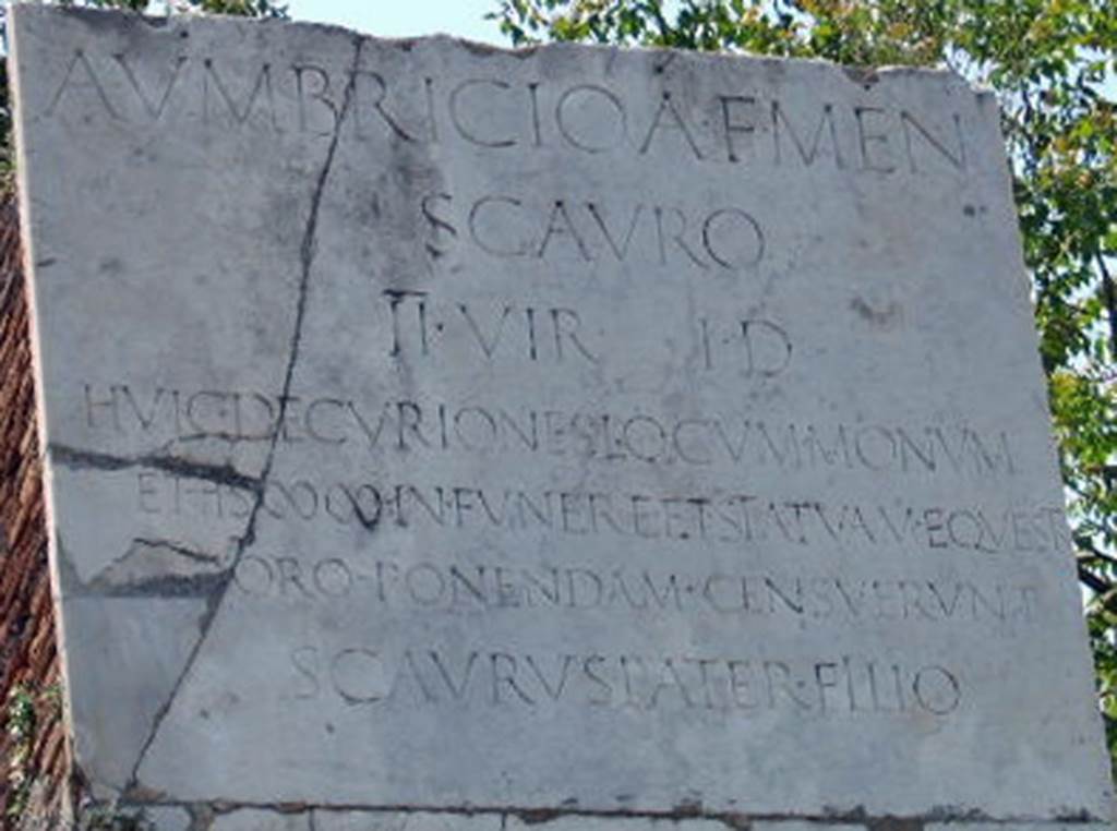 HGW17 Pompeii. May 2006. Plaque with a Latin inscription, on the east side of the tomb.

A. VMBRICIO A. F. MEN. 
SCAVRO 
II VIR I. D
HVIC DECVRIONES LOCVM MONVM
ET HS MM IN FVNERE ET STATVAM EQVESTR
IN FORO PONENDAM CENSVERVNT
SCAVRVS PATER FILIO.

According to Epigraphik-Datenbank Clauss/Slaby (See www.manfredclauss.de) this reads

A(ulo) Umbricio A(uli) f(ilio) Men(enia)
Scauro
IIvir(o) i(ure) d(icundo)
huic decuriones locum monum(entum)
et HS |(mille)|(mille) in funere et statuam equestr(em)
[in f]oro ponendam censuerunt
Scaurus pater filio      [CIL X 1024]

Mau translated this as 
‘To the memory of Aulus Umbricius Scaurus son of Aulus, of the tribe Menenia, duumvir with judiciary authority. 
The city council voted the place for a monument to this man and two thousand sesterces toward the cost of the funeral; 
They voted also that an equestrian statue in his honour should be set up in the Forum. 
Scaurus the father to the memory of his son.'
See Mau, A., 1907, translated by Kelsey F. W. Pompeii: Its Life and Art. New York: Macmillan. (p. 410-11).
