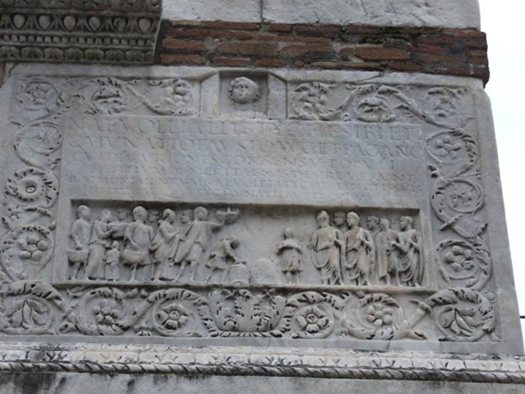 HGW22 Pompeii. December 2007. East side with carving of marble floral pattern, people and inscription.
On the panel above the people is the Latin inscription:

NAEVOLEIA .  L  LIB  TYCHE  SIBI  ET
C. MVNATIO  FAVSTO  AVG  ET  PAGANO
CVI  DECVRIONES  CONSENSV  POPVLI
BISELLIVM  OB  MERITA  EIVS  DECREVERVNT
HOC  MONIMENTVM   NAEVOLEIA  TYCHE  LIBERTIS  SVIS
LIBERTABVSQ  ET  C.  MVNATI  FAVSTI  VIVA  FECIT.

According to Epigraphik-Datenbank Clauss/Slaby (See www.manfredclauss.de) this reads

Naevoleia L(uci) lib(erta) Tyche sibi et
C(aio) Munatio Fausto Aug(ustali) et pagano
cui decuriones consensu populi
bisellium ob merita eius decreverunt
hoc monimentum Naevoleia Tyche libertis suis
libertabusq(ue) et C(ai) Munati Fausti viva fecit      [CIL X 1030]

Mau translated this as:

Naevoleia Tyche, freedwoman of Lucius Naevoleius, for herself and for Gaius Munatius Faustus, member of the Brotherhood of Augustus and suburban official, to whom on account of his distinguished services the city council, with the approval of the people, granted a seat of double width. 
This monument Naevoleia Tyche built in her lifetime also for the freedmen and freedwomen of herself and of Gaius Munatius Faustus.

See Mau, A., 1907, translated by Kelsey, F. W., Pompeii: Its Life and Art. New York: Macmillan. (p. 422-3).