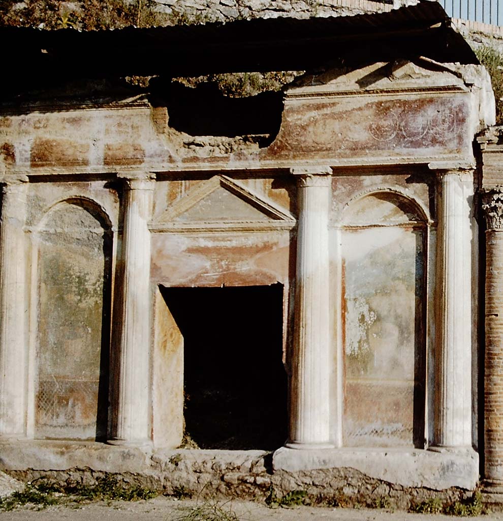 Pompeii Porta Nocera. 1959. Tomb 19ES. Richly decorated front of tomb with four columns, two top pediments, a lunette and stucco bordered panels.
The front is richly decorated with garden paintings showing fences, marble crater fountains and shrubbery at the top of which are birds.
Above the columns and below the top pediments are alternating and connected spirals of clovers and palmettes on a red background.
See D’Ambrosio, A. and De Caro, S., 1983. Un Impegno per Pompei: Fotopiano e documentazione della Necropoli di Porta Nocera. Milano: Touring Club Italiano. 19ES.
Detail from photo by Stanley A. Jashemski.
Source: The Wilhelmina and Stanley A. Jashemski archive in the University of Maryland Library, Special Collections (See collection page) and made available under the Creative Commons Attribution-Non-Commercial License v.4. See Licence and use details.
J59f0365