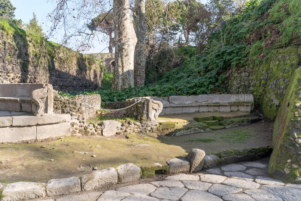 SGF Pompeii. January 2023. Looking east towards entrance to the tomb enclosures, centre, and tomb SGF, on right.
A drain set in the kerb in front of the enclosure entrance and the worn steps set in the centre of the schola are now visible. 
Photo courtesy of Johannes Eber.

