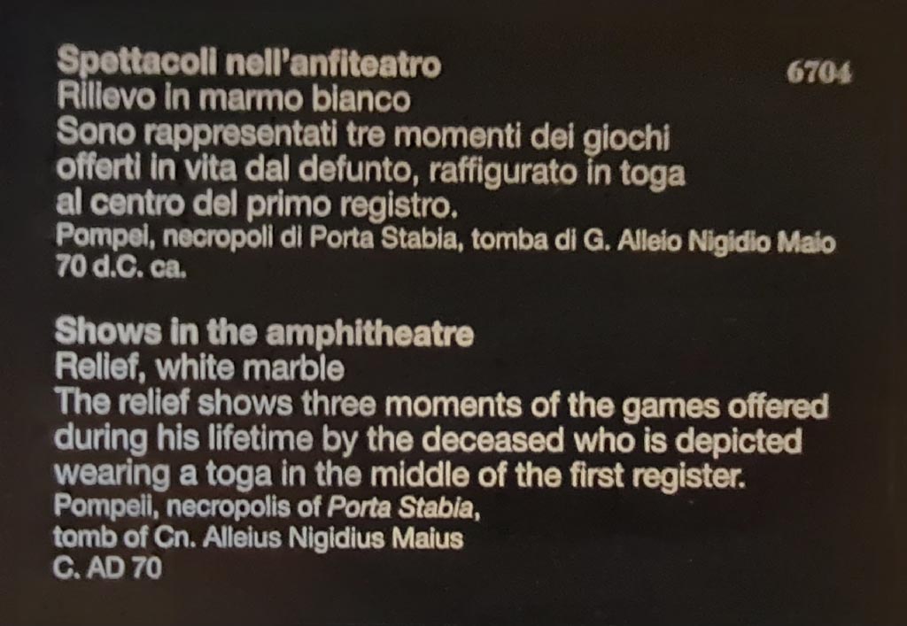 SG6 Pompeii. April 2023. Descriptive card for relief inv. 6704 in Naples Archaeological Museum.
Shows in the amphitheatre. The white marble relief shows three moments in the games offered during his lifetime by the deceased who is depicted wearing a toga in the middle of the first row.
This card clearly identifies the tomb as being that of Cn. Alleius Nigidius Maius.
Spettacoli nell’anfiteatro. Il rilievo in marmo bianco rappresentati tre momenti dei giochi offerti in vita dal defunto, raffigurato in toga al centro del primo registro.
Questa carta identifica chiaramente la tomba come quella di G. Alleio Nigidio Maio.
Photo courtesy of Giuseppe Ciaramella.