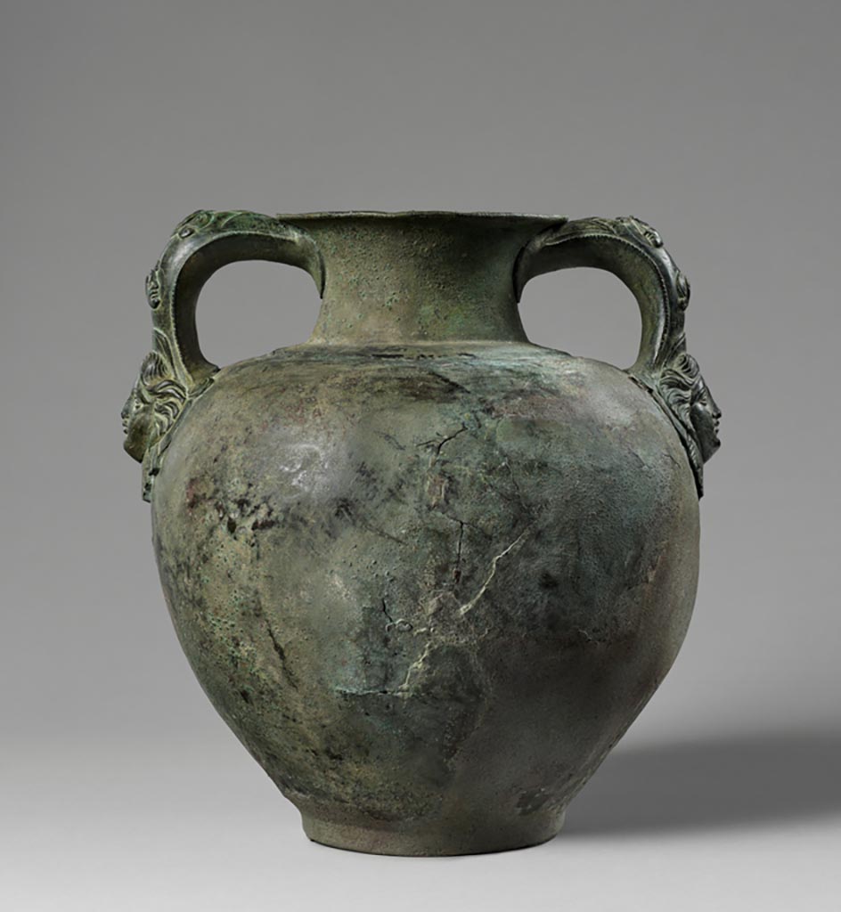 Discovered in a villa in Boscoreale. Bronze amphora with two handles each with a satyr and a maenad.
Digital image courtesy of the Getty's Open Content Program. Now in the Getty Museum, inventory number 72.AC.144.
The handles of this otherwise undecorated amphora (storage jar) take the form of two male heads in profile—one facing left, the other right. Appliques in the shape of frontal female heads attach the base of each handle to the vessel. The figures represent satyrs and maenads, companions of the wine god Bacchus.
Vessels of this type were frequently used to hold wine at banquets. This amphora was discovered in a villa at Boscoreale or in the vicinity, although the exact findspot is unknown. 
