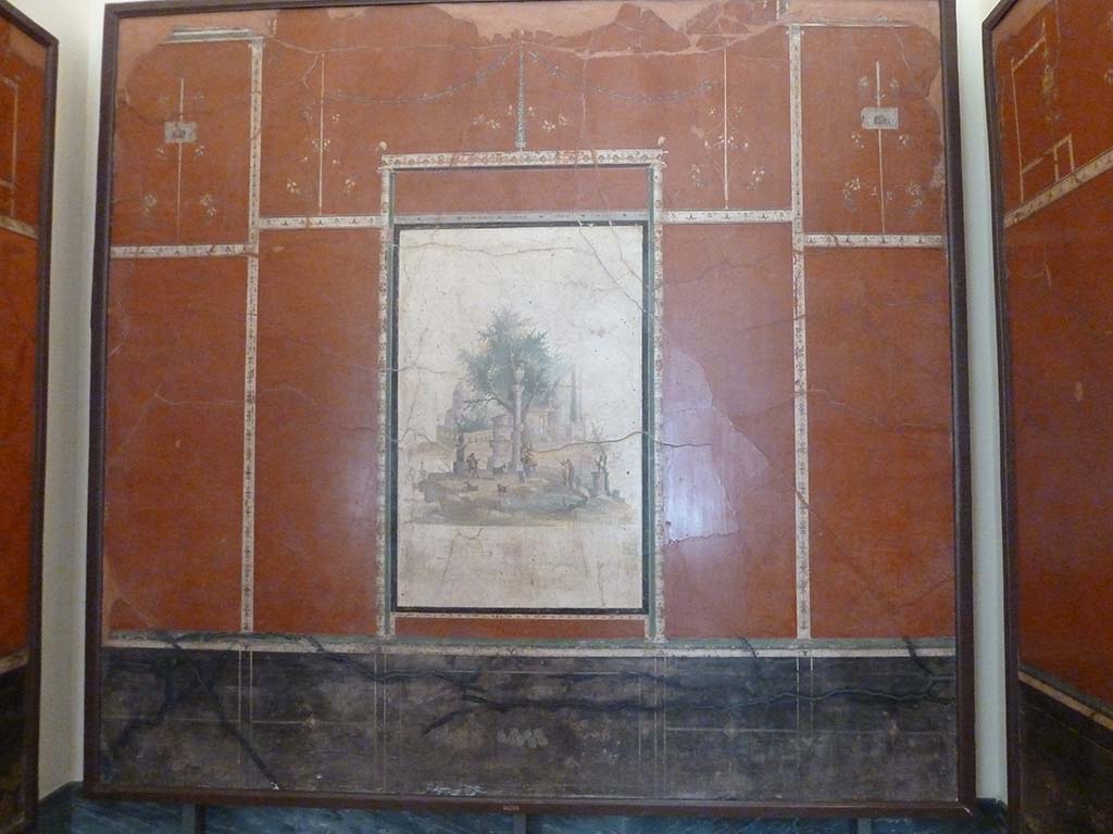 Villa Agrippa Postumus, Boscotrecase. May 2010. Room 16, north (rear) wall.
Now in Naples Archaeological Museum. Inventory number 147501.
A still-life depicting figs can be seen in the black ground dado/plinth of the rear wall.
At the centre of the slender framed aedicule is a sacred landscape with shepherds and goats near a circular shrine and votive column, small panels with theatrical masks, delicate candelabra and branches with flowers complete the decorative ensemble in the upper zone.