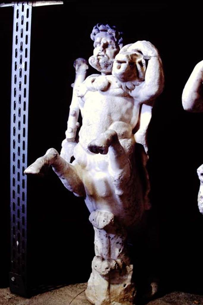 Oplontis Villa of Poppea, 1977. One of a group of four centaurs, a male holding a club with a small boar on his shoulder. 
Two centaur fountains had been on each side of the passageway.
There was no evidence of pipes, so they had not been used as fountains in their final location.
Photo by Stanley A. Jashemski.   
SAP inventory number 70068.
Source: The Wilhelmina and Stanley A. Jashemski archive in the University of Maryland Library, Special Collections (See collection page) and made available under the Creative Commons Attribution-Non Commercial License v.4. See Licence and use details.
J77f0340
According to De Caro, a group of four centaurs were found under portico 33 on 17th February 1970. 
When they were found, they were very badly damaged. Heads and limbs were mostly detached and it was necessary to provide patient and pain-staking work of re-composition. 
See De Caro, S.1976. Sculture dalla villa di Poppea in Oplontis (p.198) in Cronache Pompeiane, II, 1976, (p.184-225)

