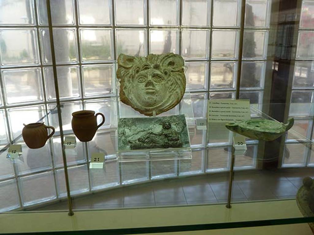 Boscoreale, Villa rustica in via Casone Grotta, proprietà Risi di Prisco. 
Finds from villa, from right to left.
18. Thin-walled tankard or jug
19. Thin-walled tankard or jug
17. Terracotta Antefix 
21. Silver relief, with depiction of a female figure relaxing
20. Glazed terracotta lamp
Now in Boscoreale Antiquarium. Photo courtesy of Michael Binns.
