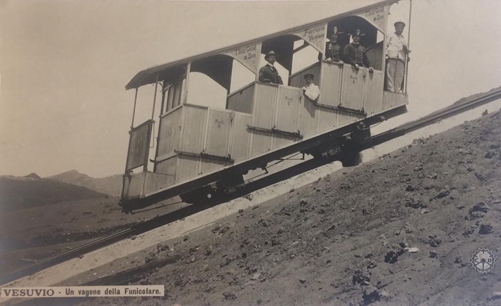 Postcard showing a Wagon of the Vesuvius Funicular, with handwritten note on rear- “The 1904 Funicular only lasted 2 years”.  
Photo courtesy of Rick Bauer.
This photo must be dated between 1904 when the cars were introduced and 1906 when they were destroyed..
The funicular was modernised at the same time as Cook’s Pugliano to Vesuvius light railway was opened in 1904.
The monorails had been removed and the track was now a one metre gauge single track with a central passing loop.
These cars were new in 1904 and seated 18 with 6 standing. 
Thomas Cook and Son’s name is on the upper part of the structure. The wording on each of the three doors is “Posti 6” (6 places).
Two years later, in a tremendous eruption, on 7 and 8 April 1906 the lower and upper station, the equipment, the machinery, the two funicular cars were destroyed.
Everything was buried under a 20-30m high ash blanket.
Although the light railway as far as the hotel Eremo was quickly dug out, the funicular had to wait. 
Only in 1909, according to the project of the engineer Enrico Treiber, were the works for a new funicular ended and it reopened in 1910.
